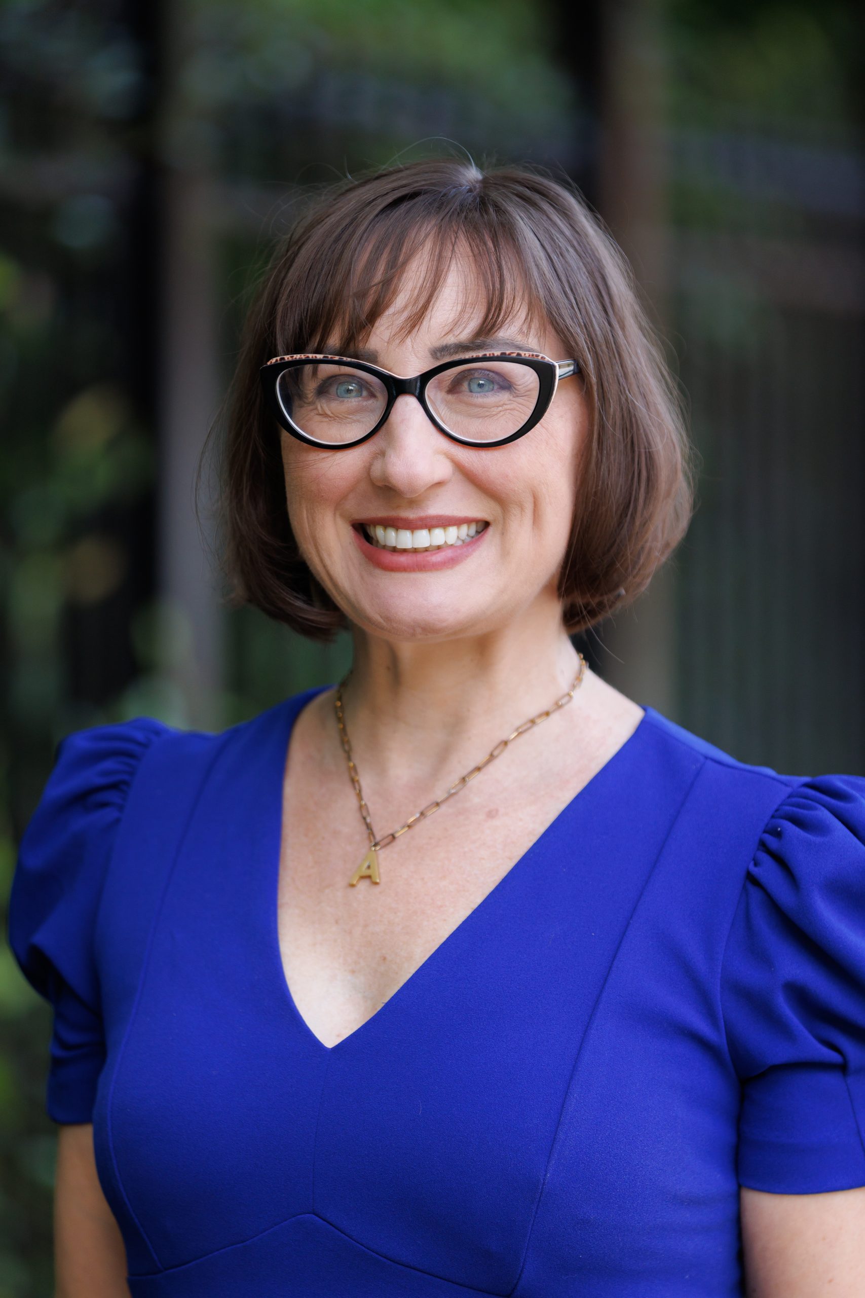 Dr. Prohaska smiling to the camera, wearing a blue top and glasses.