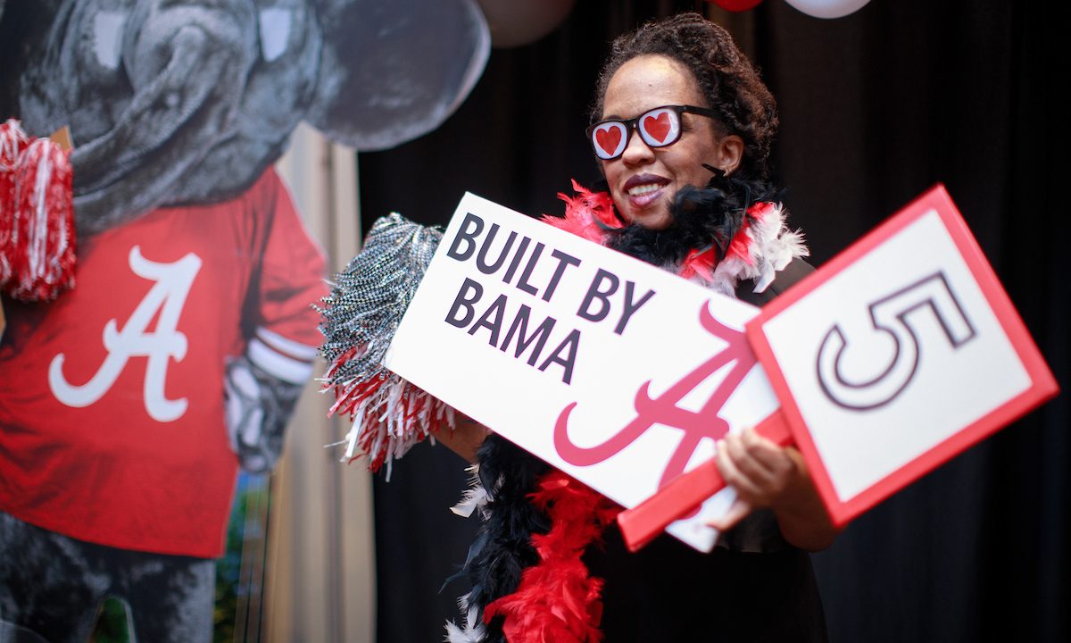 Woman wearing funny glasses holding sign that says Built by Bama 5